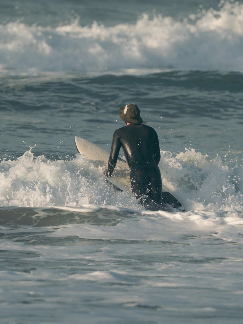 Surfer in the Driftwood hat wading into the whitewater, board in hand